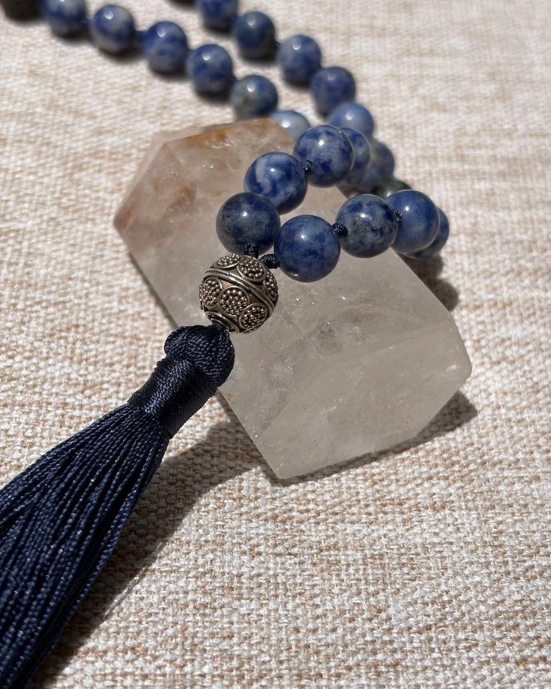 Blue beaded necklace with tassel on a crystal stone against a textured beige background