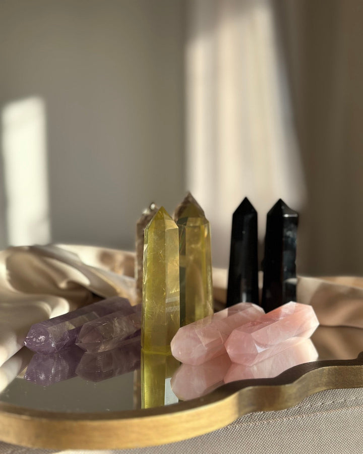 Set of crystals including amethyst, green crystal, black crystal, and pink crystal on a reflective surface with a neutral background.