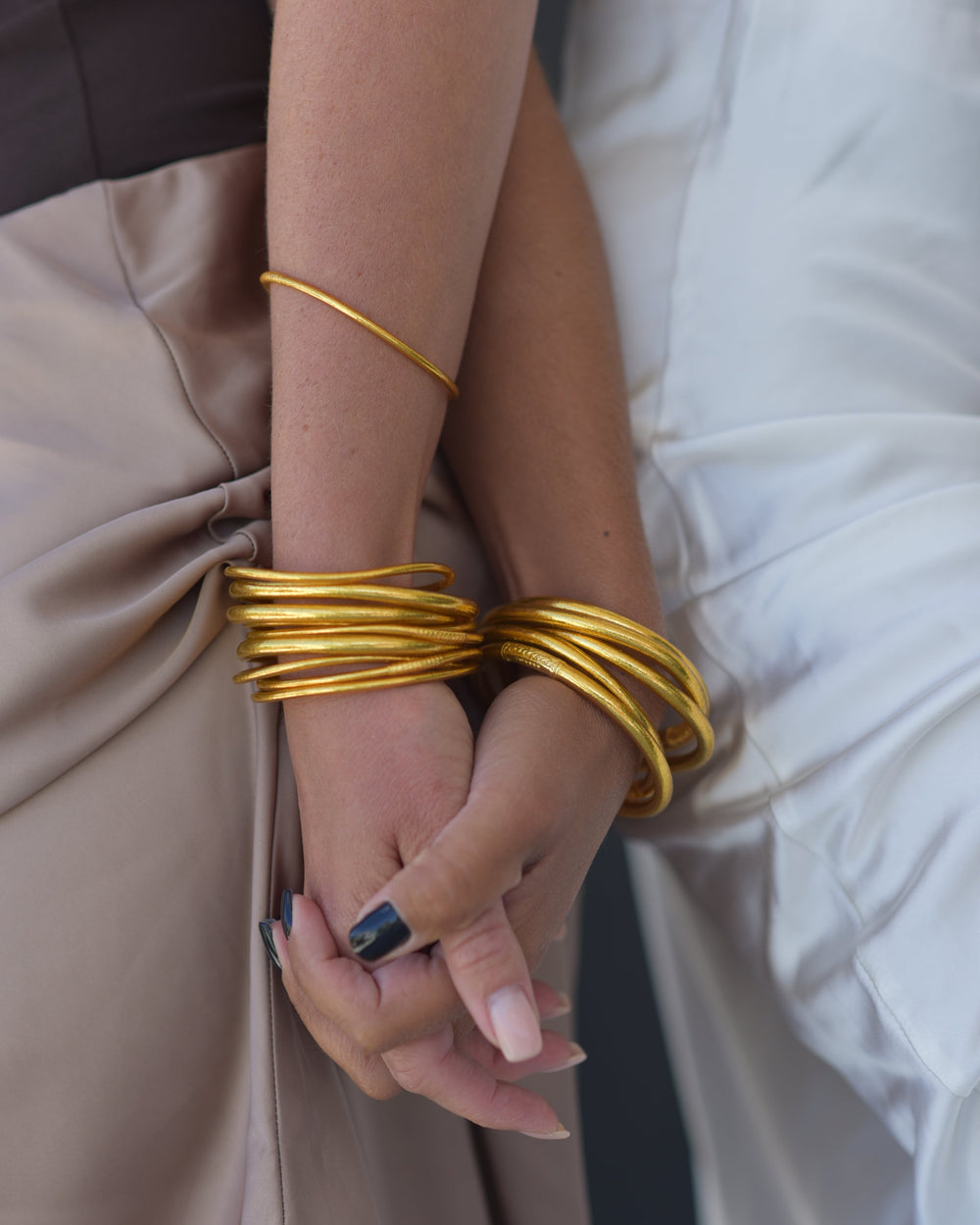 Close-up of a person's arm with gold bracelets on a neutral background