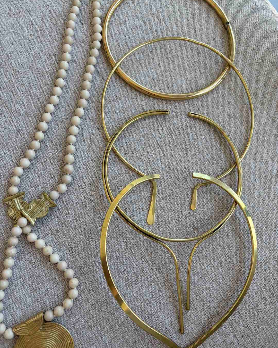 Gold hoop neck chokers and a beaded necklace on a textured surface