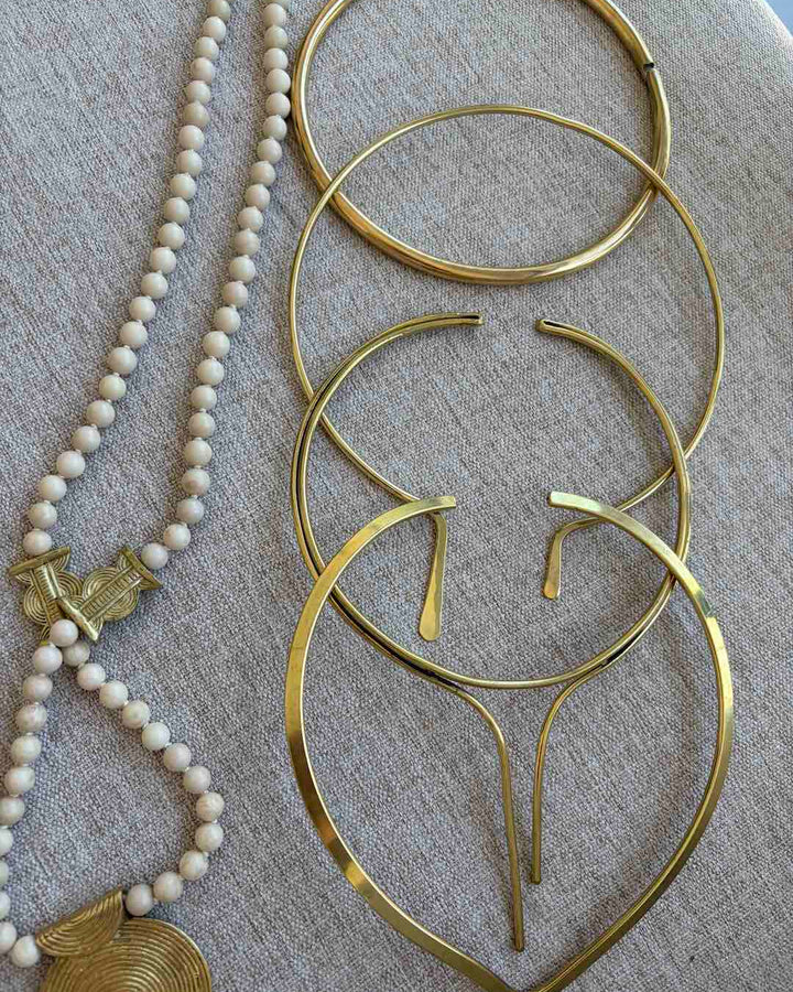 Gold hoop neck chokers and a beaded necklace on a textured surface