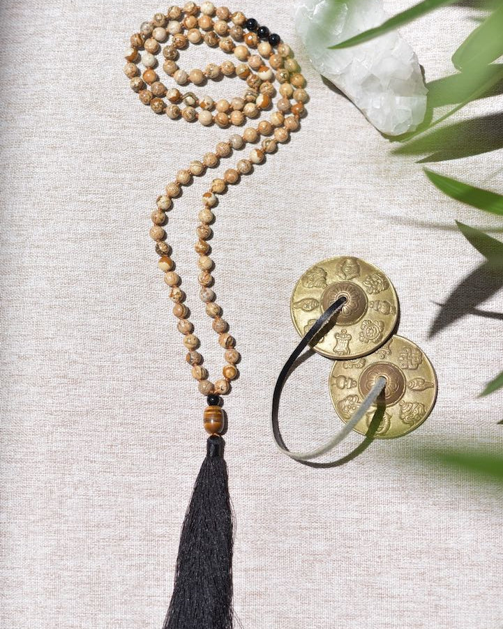 Jasper beaded necklace with tassel and brass pendants on a textured surface.