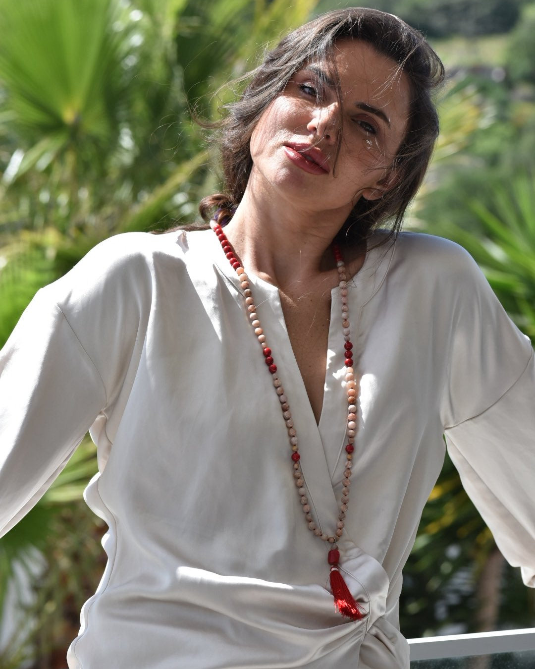 Person wearing a white outfit with a long necklace in a natural setting