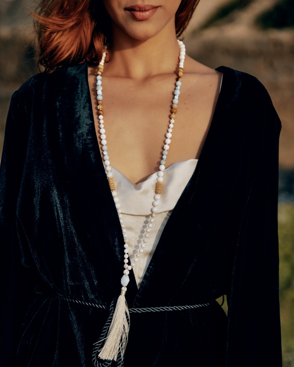 Person wearing a black velvet robe with a long necklace and tassel, standing outdoors.