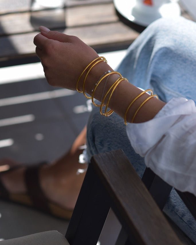 Person wearing gold bracelets on a wooden chair with a blurred background
