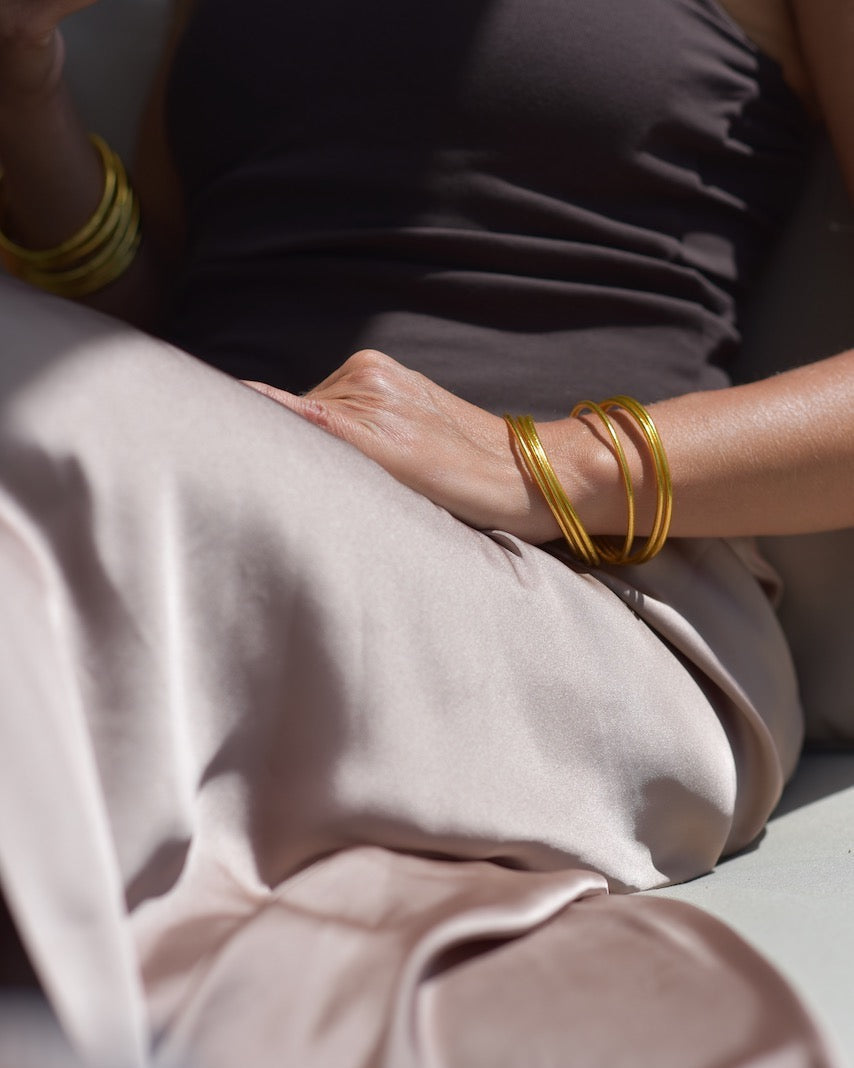 Person wearing gold bracelets on a neutral background
