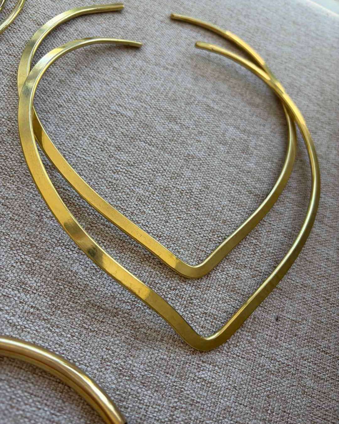 Gold hoop neck chokers on a textured beige surface