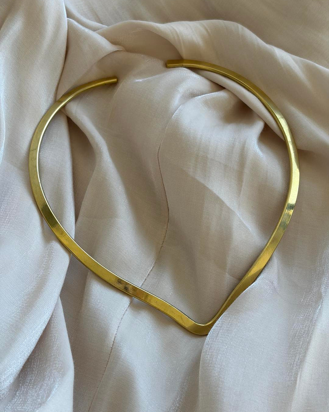 Gold choker necklace on a beige fabric background