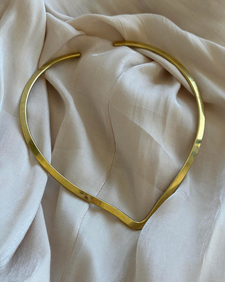 Gold choker necklace on a beige fabric background